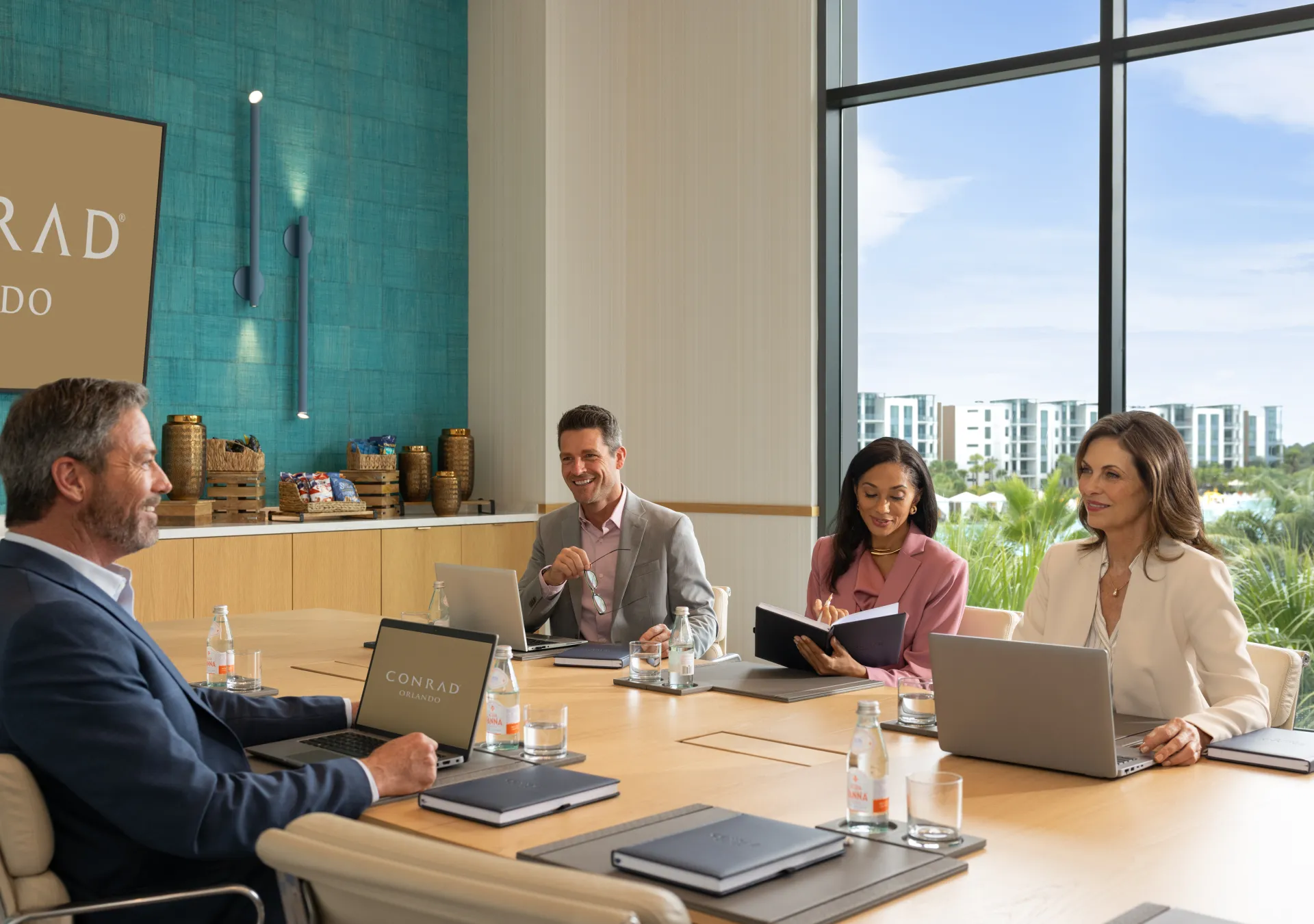 Four professionals in business attire having a meeting around a conference table with laptops and notebooks in the Lotus Boardroom at Conrad Orlando.