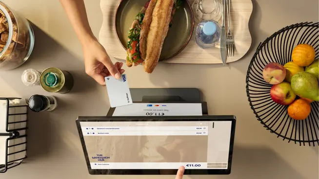 Person paying with a contactless card on an Adyen payment terminal at a restaurant.